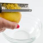 zesting a lemon with a microplane zester into a glass bowl
