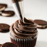 Oreo cookies and cream frosting being piped onto a cupcake