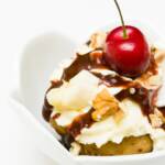 A fully-prepared banana split cupcake with banana whipped cream, chocolate drizzle, nuts, and a cherry