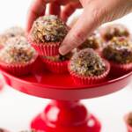 Sugar plums in red mini cupcake liners on a red cupcake stand with a hand selecting one