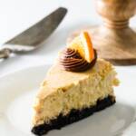 A slice of orange cheesecake with a cake stand in the background