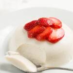 panna cotta on a plate served with macerated strawberries with a spoonful removed