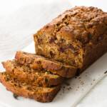 Date nut bread on a white serving plate, partially sliced