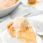 Slice of honey pie on a white plate with a scoop of ice cream on top and a pie in the background