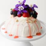 pavlova covered with whipped cream, fresh fruit, and flowers