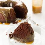 Slice of chocolate whiskey cake with Bundt cake and jar of whiskey sauce in the background