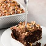 Piece of chocolate carrot cheesecake on a white plate with a fork in it and the baking dish in the background